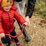 Joyful child riding a bike with parent on a gravel path, enjoying family time outdoors.