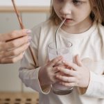 A caucasian child drinks a smoothie using a metal straw at home.