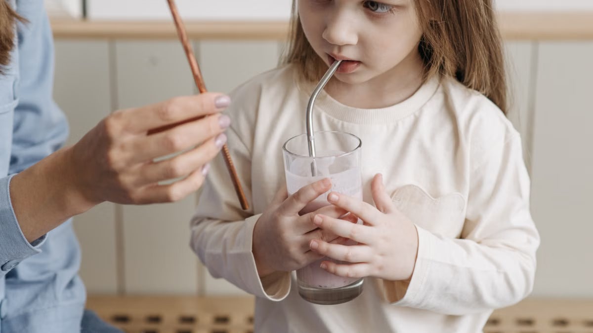 A caucasian child drinks a smoothie using a metal straw at home.